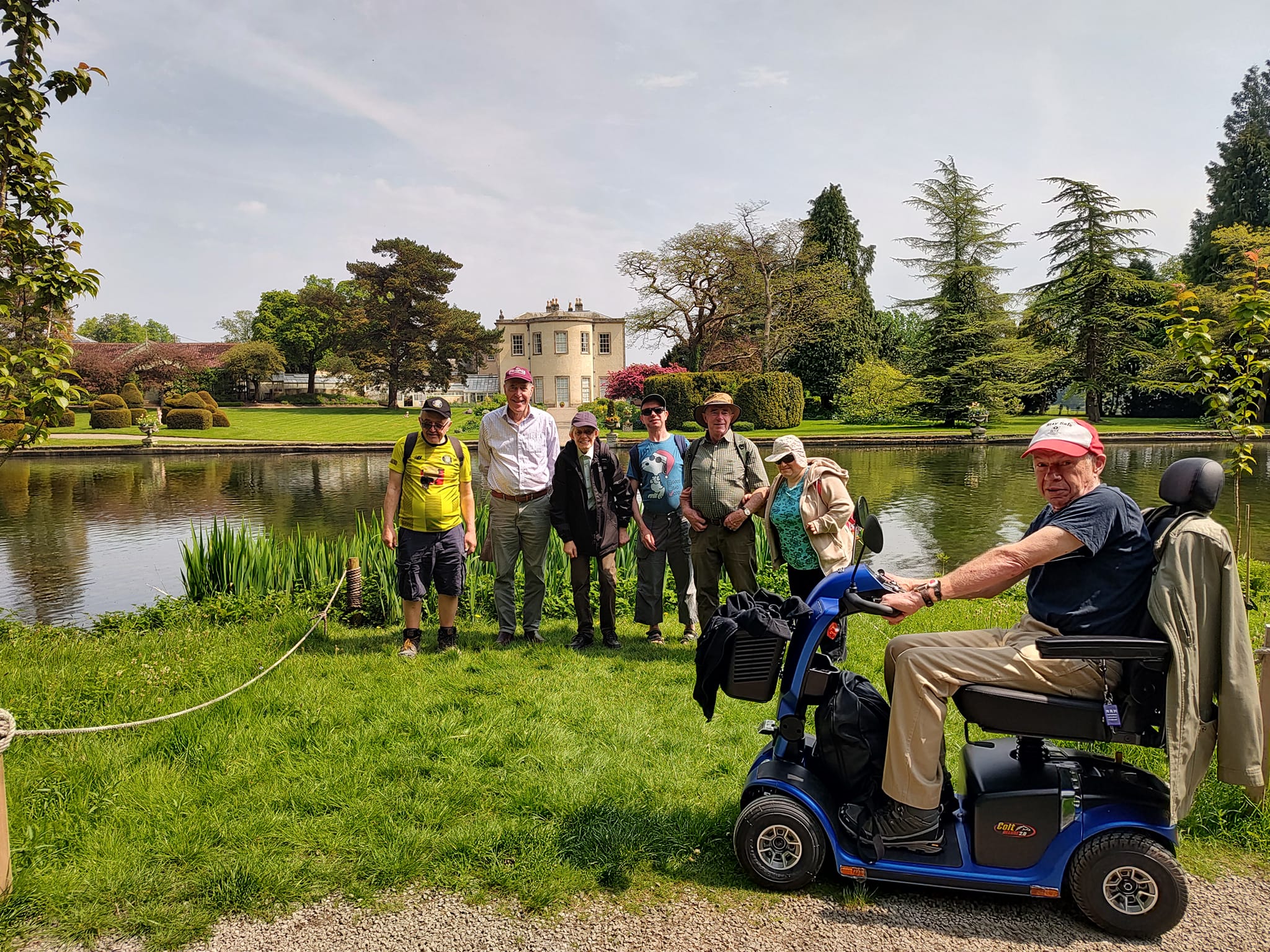 A man on a mobility scooter standing in front of a lake with people in the background