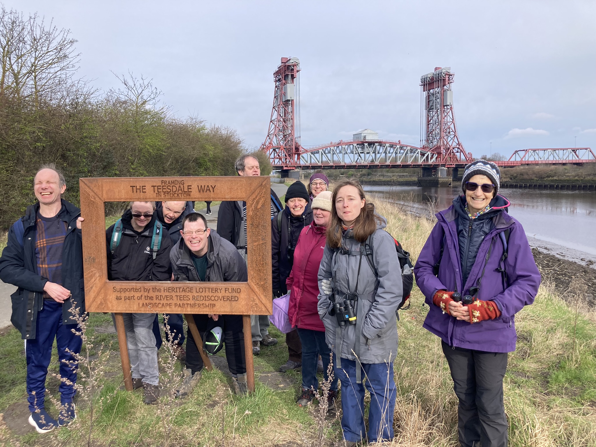 A group of people standing by a river with a bridge in the background